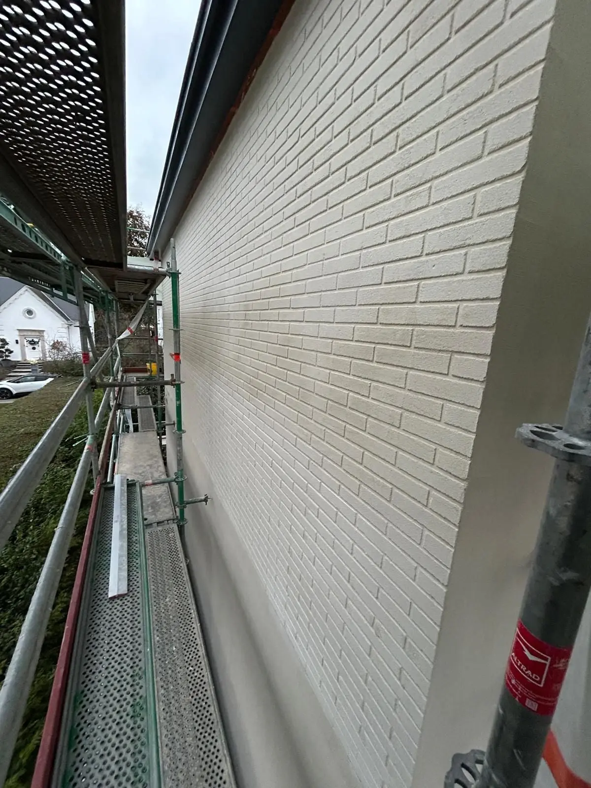 Un long mur à l’aspect brique, vu depuis l’échafaudage, à Auderghem