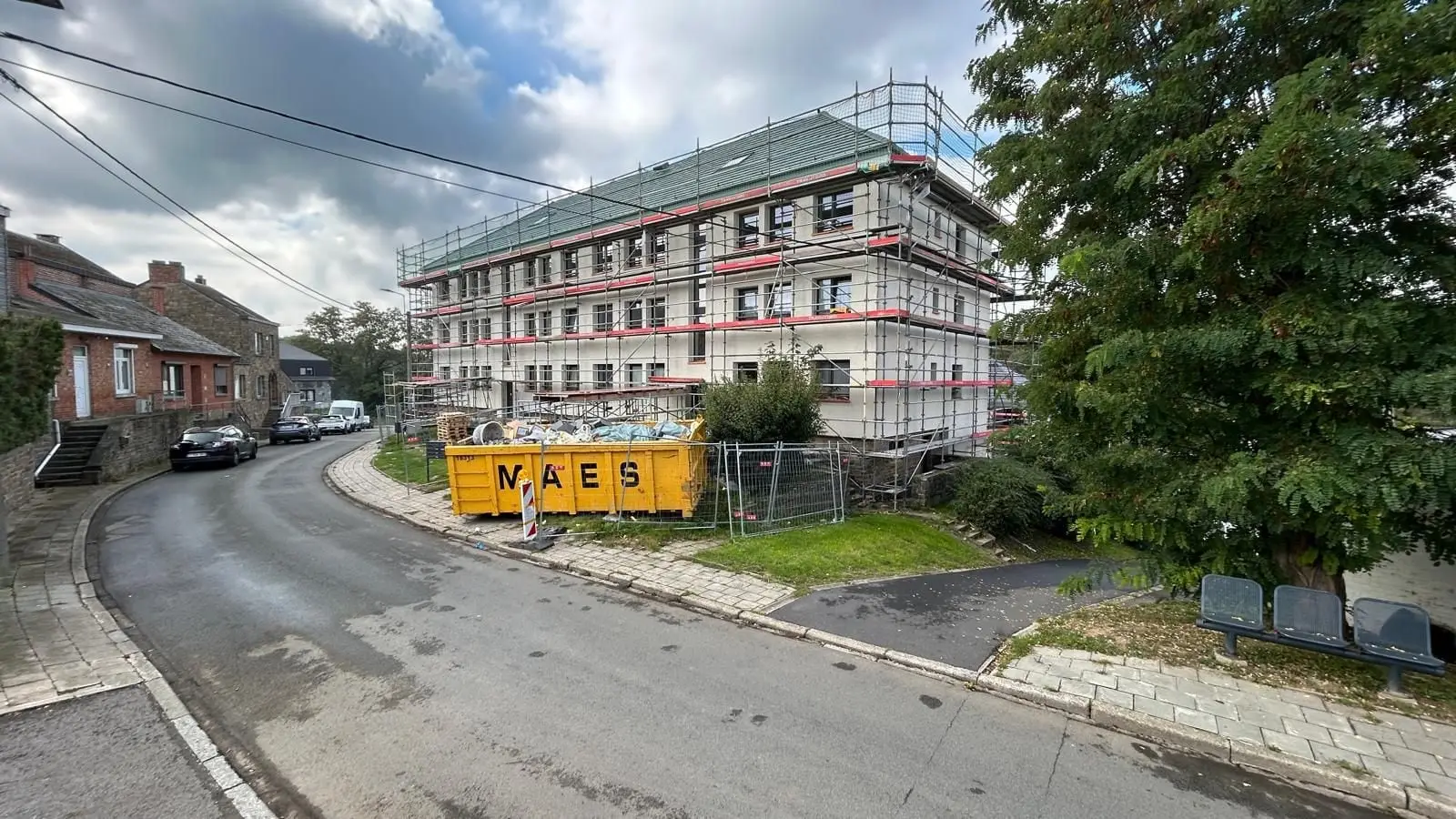 Le même immeuble sous échafaudage, une benne de chantier devant, à Namur